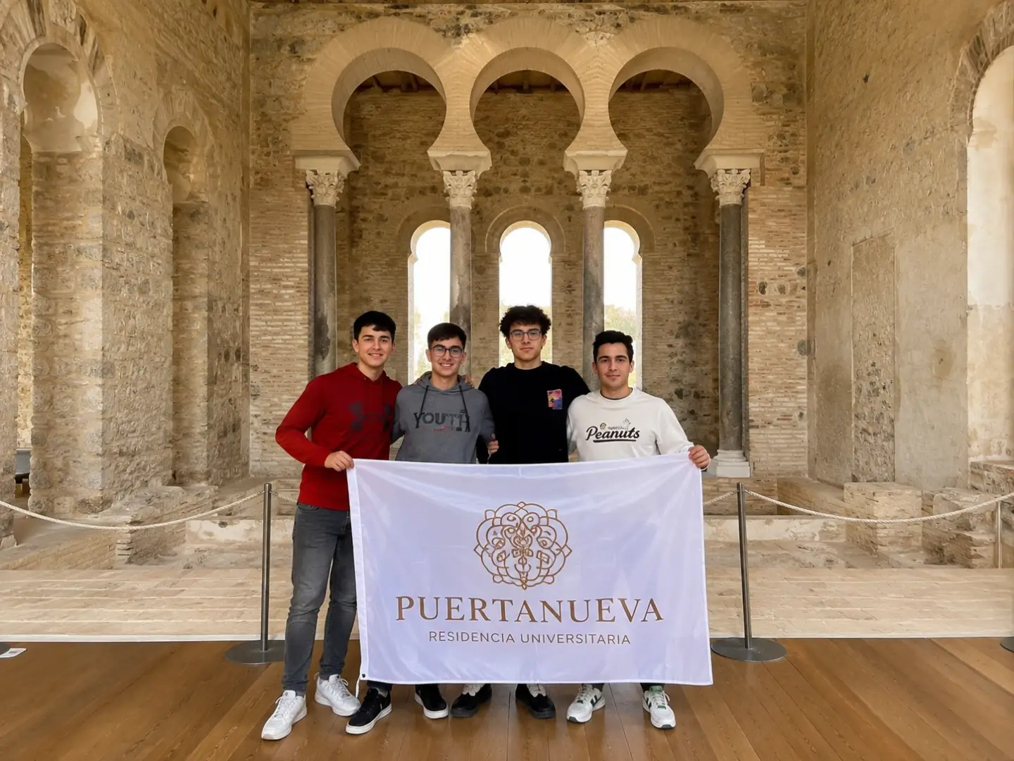 Visita cultural de residentes de Puertanueva a Medina Azahara: cuatro estudiantes sostienen la bandera de la residencia bajo los tres arcos califales